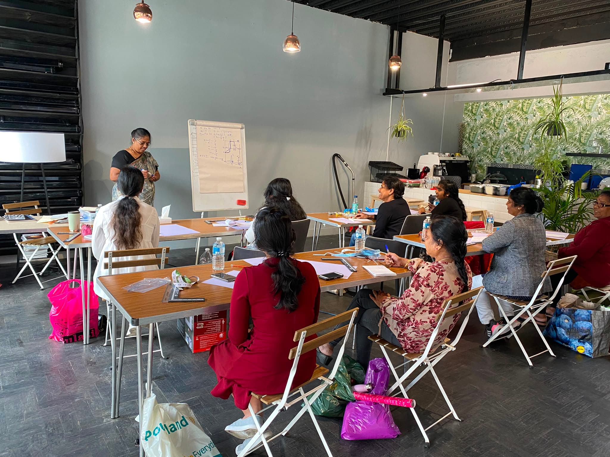 A tailoring teacher demonstrating pattern drafting to students in a sewing workshop